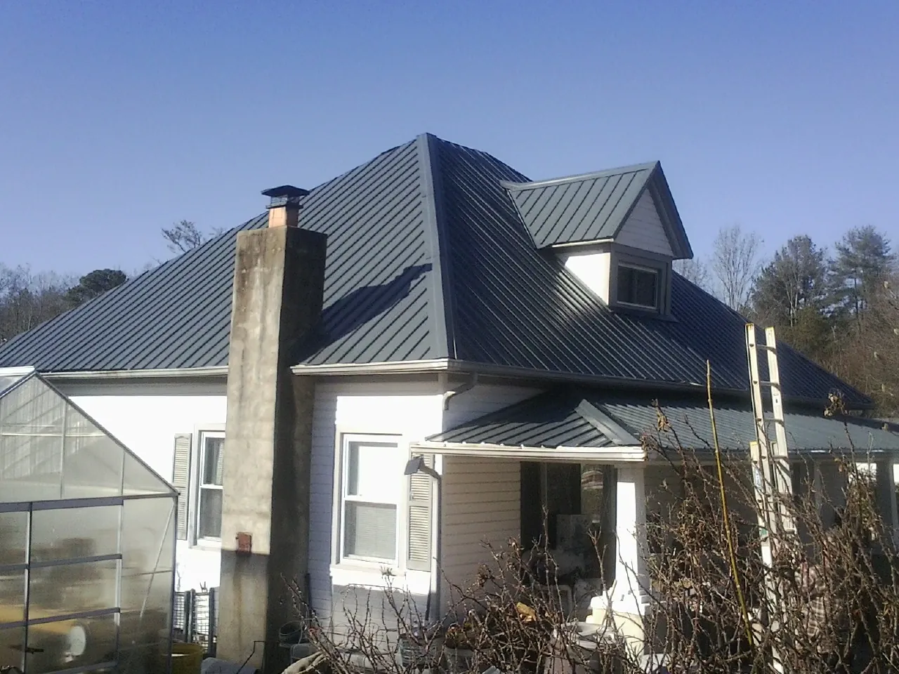 Dark blue standing seam metal roof on a white farmhouse with dormer — Slate & Tile Roof Repair by Roofing Brothers in Pennock