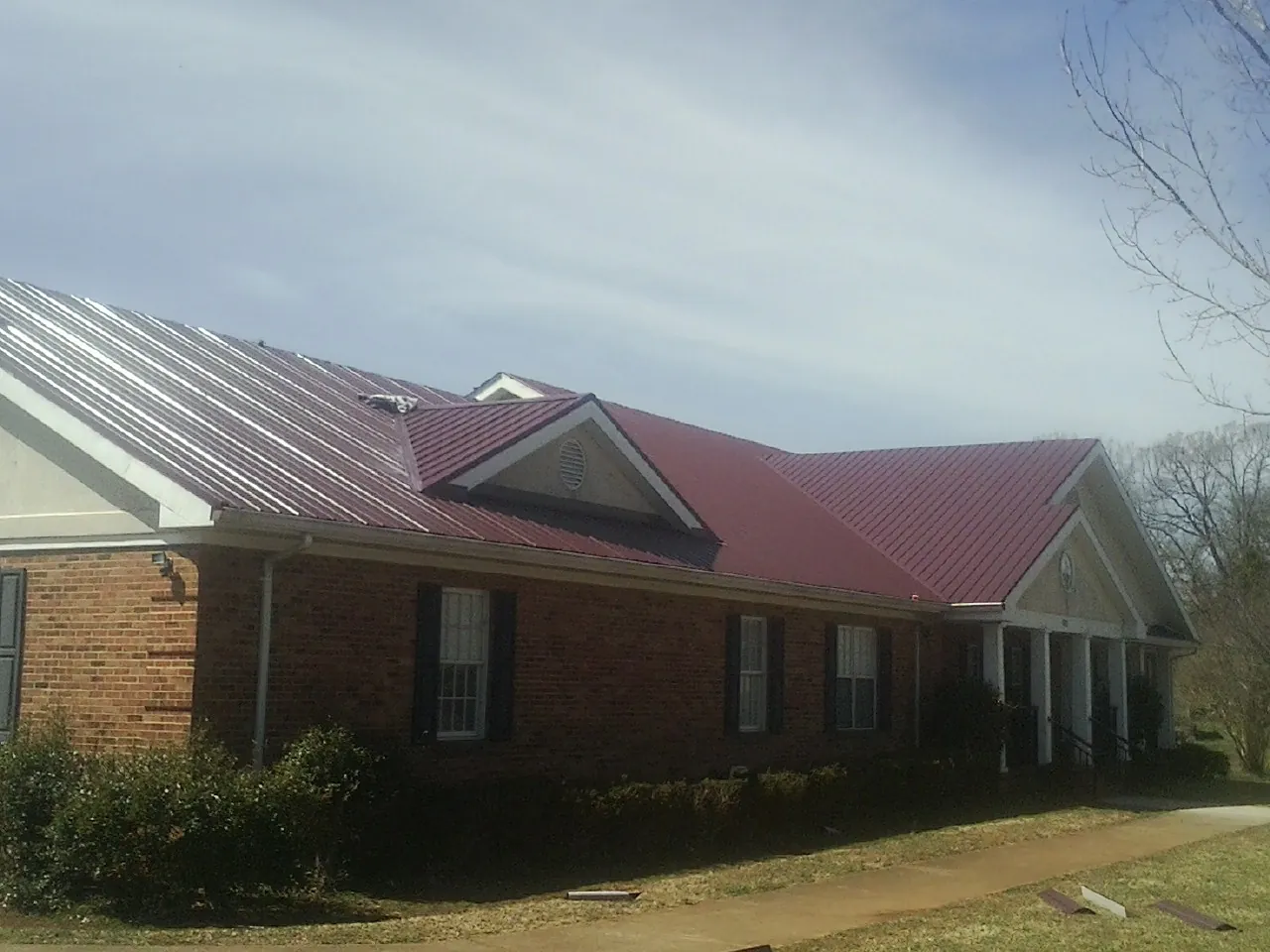 Red metal roof with gabled entries on a long brick building, from a Hail Damage Roof Repair job in Pennock