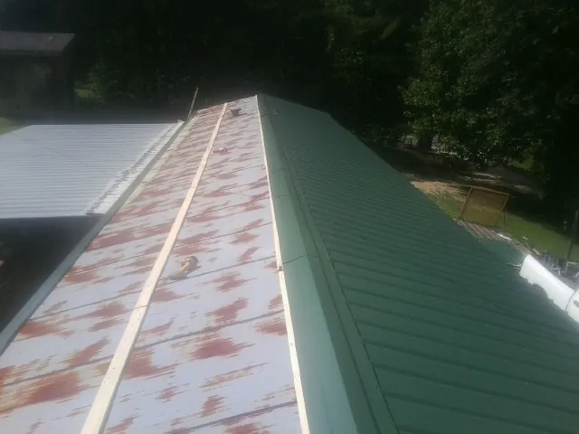 Old rusted panels beside newly installed green metal roofing — Wind Damage Roof Repair by Roofing Brothers in Pennock