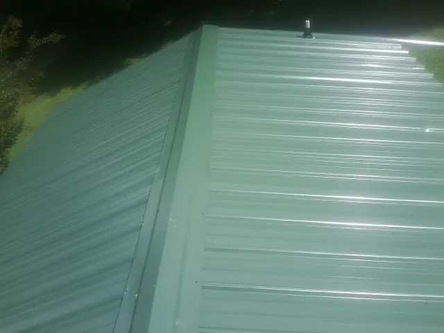 New green metal panels meeting at the ridge of a roof — Flat Roof Repair work by our crew in Pennock