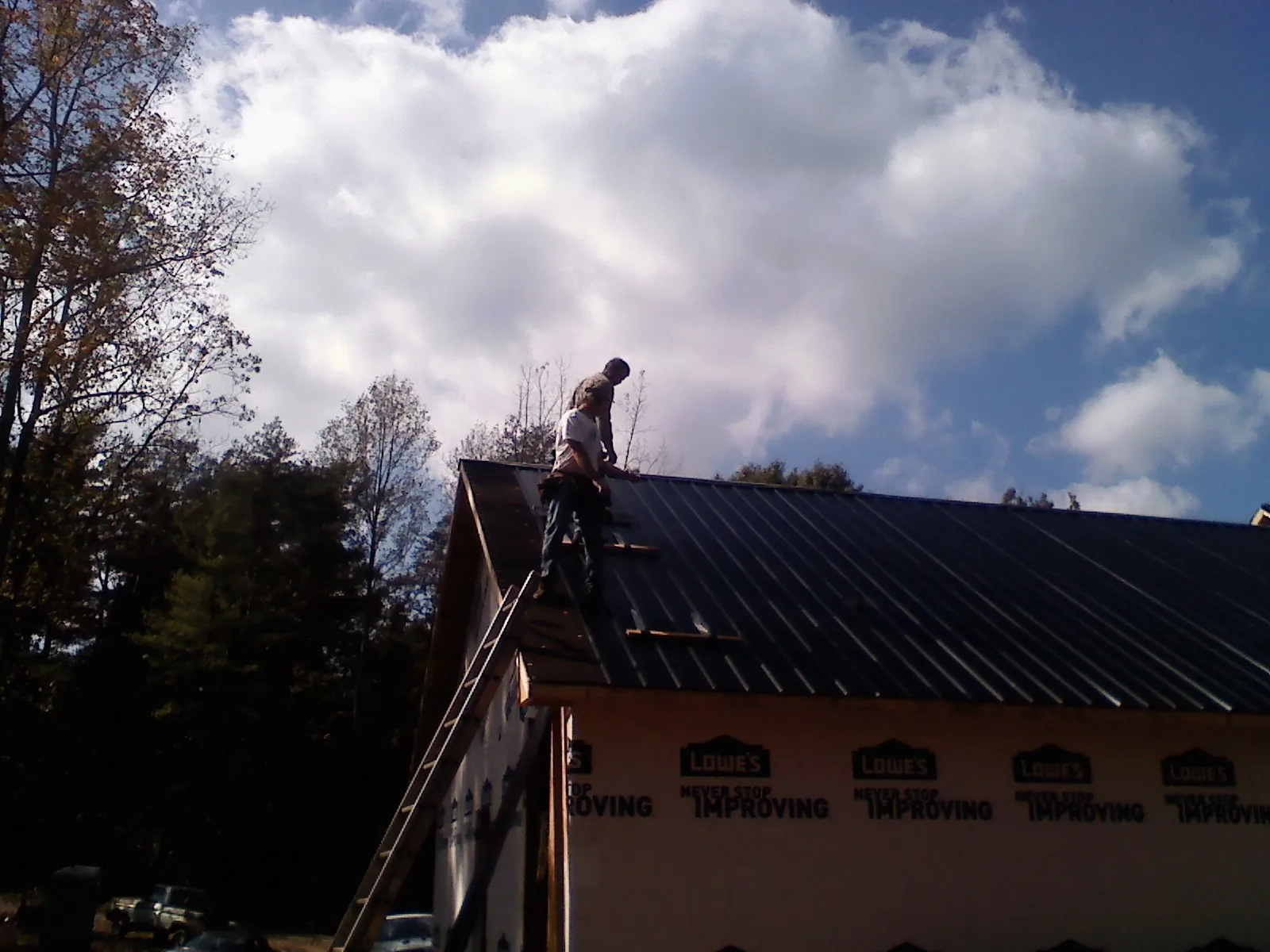 Roofer fastening dark metal panels high against a cloudy sky, from a Roof Inspection job in Pennock