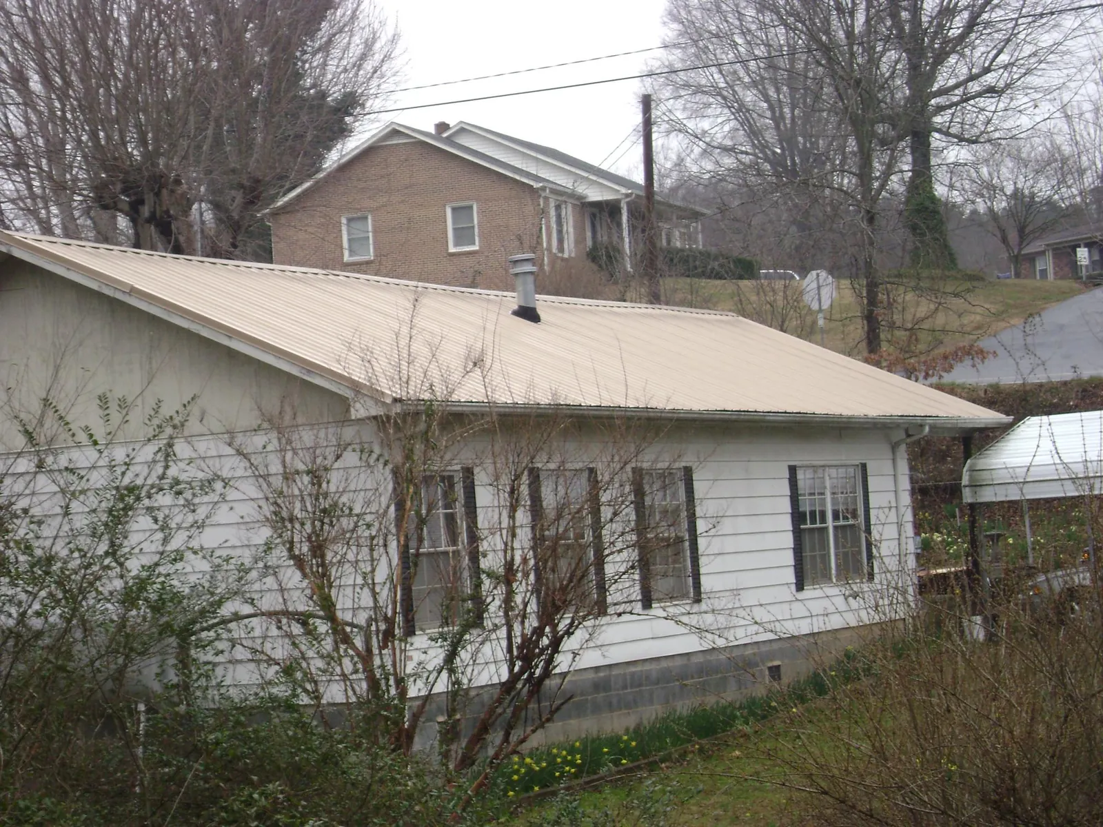 Tan metal roof on a white sided house set into a hillside — Commercial Roofing by Roofing Brothers in Pennock