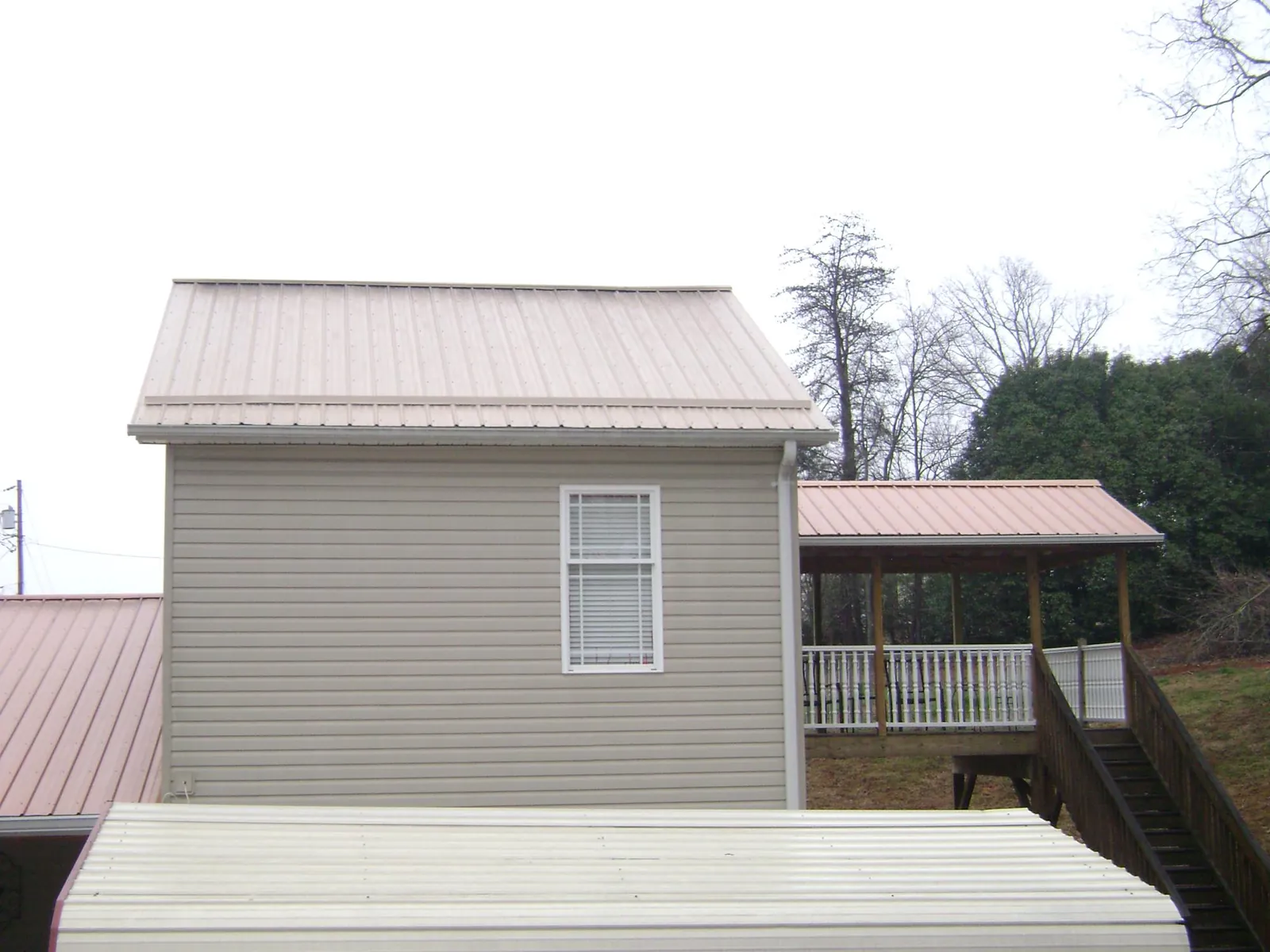 Tan metal roofs on a two story addition and attached porch, from a Roof Replacement job in Pennock